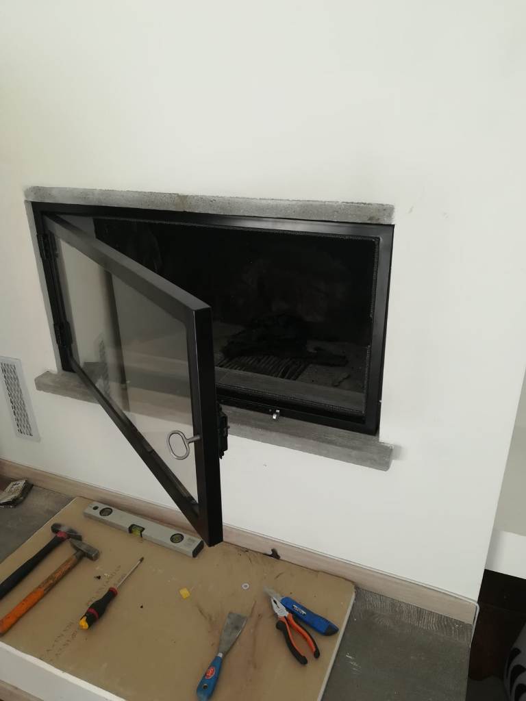 chiusura di un camino aperto con vetro ceramico e sportello aperto in fase di posa.